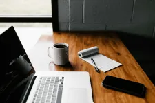 A table with a laptop, a coffee cup, a smartphone and a notepad. Photo.
